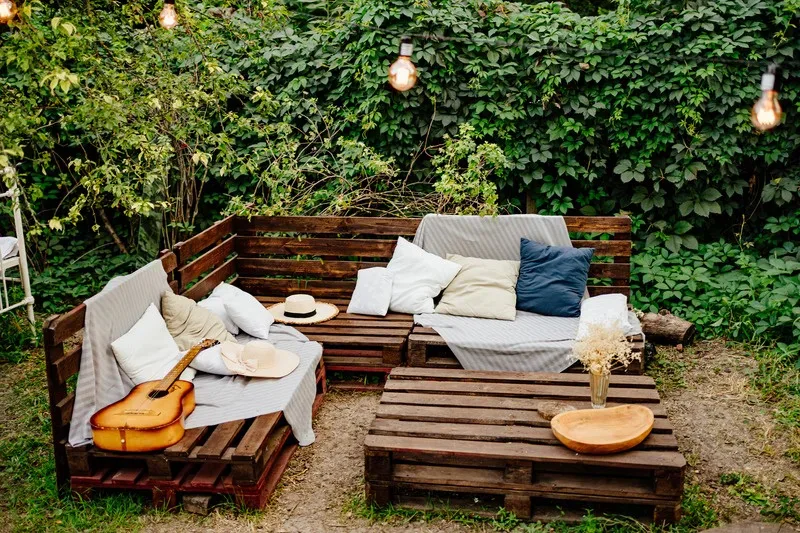 An outdoor lounge with cushions, lanterns and a guitar against a wall of green