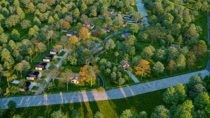 Render of farmhouses among trees beside a road, seen from above