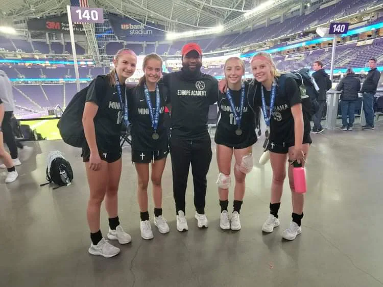 Coach Mulenga posing with four athletes wearing medals inside U.S. Bank Stadium.