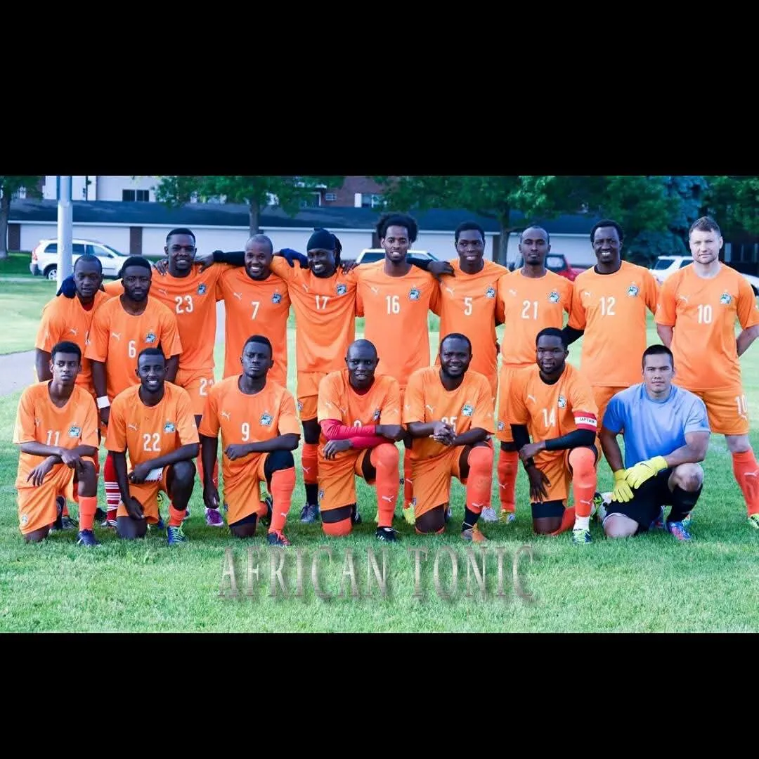 Men's soccer team in orange uniforms posing on a grass field.